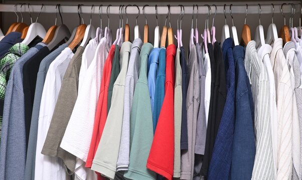 A close-up view of a organized wardrobe featuring a varied selection of men casual garments suspended on a metal handing rod