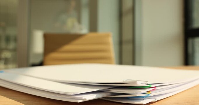 In a modern office, neatly stacked papers with colorful clips sit on a wooden desk. The warm natural light highlights the papers, creating a calm atmosphere of organization and efficiency.