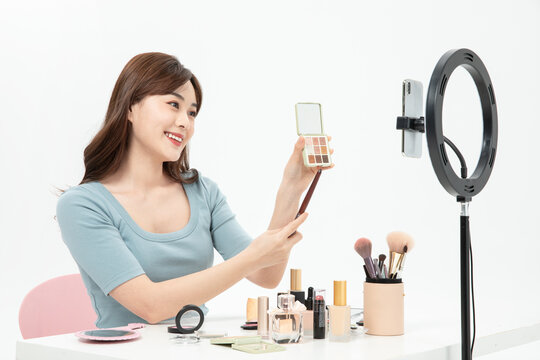 Beautiful female streamer applying makeup during online live broadcast