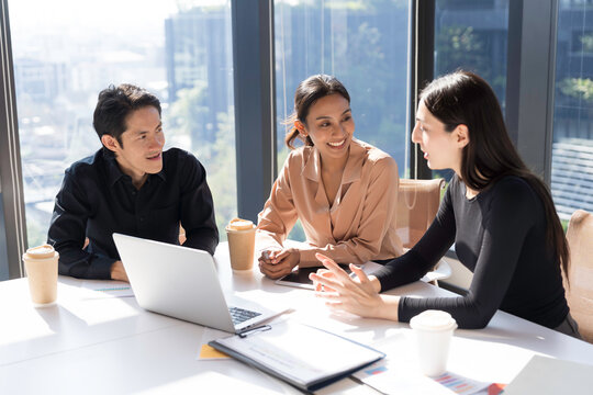 Diverse corporate colleagues brainstorming, discuss together project with laptop computer, document in office meeting. Male, female employees business meeting in office conference room