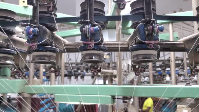 Circular Knitting Machine Yarn Feeders Operating In Garment Factory
Close up view of yarn feeders on a circular knitting machine in operation at a textile garment factory. White yarn threads feeding i