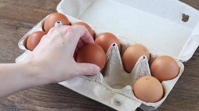 Woman Hand Sorting Fresh Brown Eggs in Cardboard Box on Wooden Background. Cooking Preparation