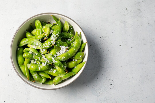Fresh steamed edamame soybeans served in a bowl with coarse sea salt on a light textured background.