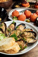 Delicious cooked mussels in a creamy sauce with fresh parsley, served with bread slices and arancini croquettes on a wooden table. © pavel siamionov