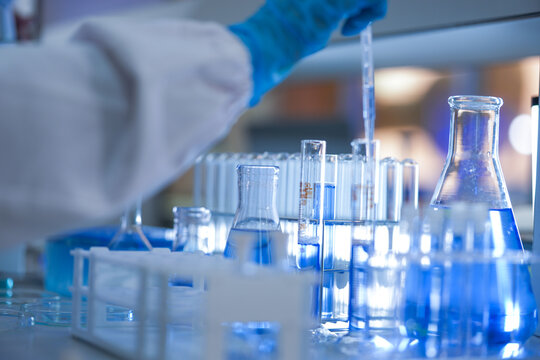 The gloved hands of a medical research scientist holding the pipette still over the tubes inside a busy medical diagnostics laboratory, in a clean and modern laboratory.
