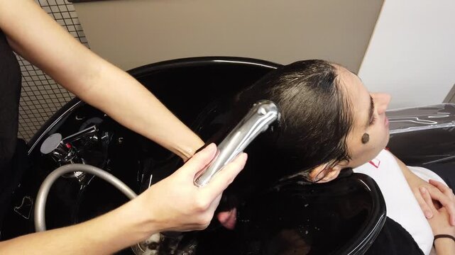 A hairdresser washing a client's long hair in a professional salon sink