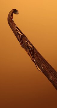 Macro vertical view of shiny oil coating a vanilla bean pod on warm background