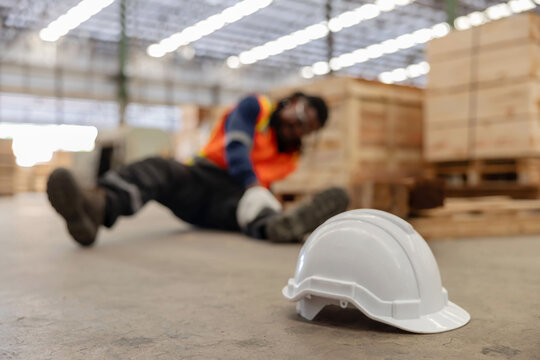 Close-up on white hard hat with blurred injured factory worker on the floor
