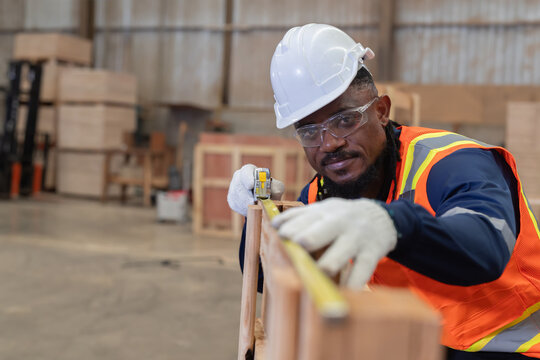 Worker measures wood in a warehouse during the day while wearing safety gear