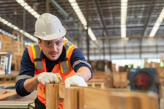 Worker measures wood in a warehouse during the day while wearing safety gear