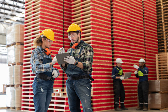 Workers discussing tasks in a warehouse with wooden pallets stacked in the background
