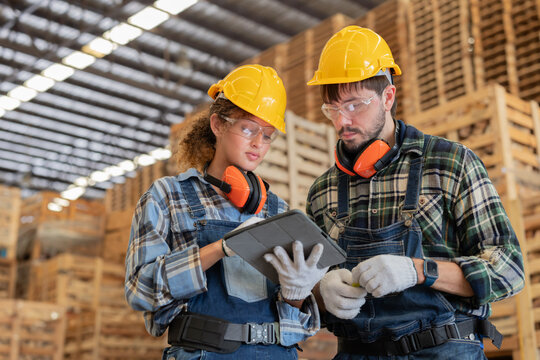 Workers discuss tasks in a warehouse with pallets stacked high in the background