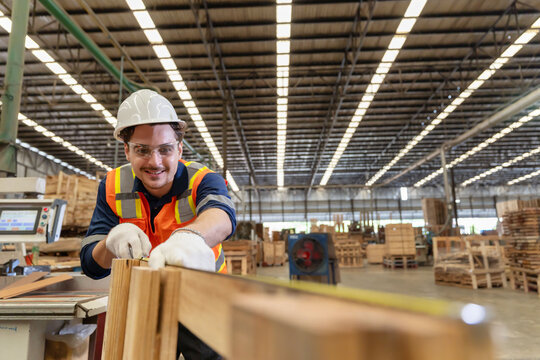 Worker measures wood in a warehouse during the day while wearing safety gear