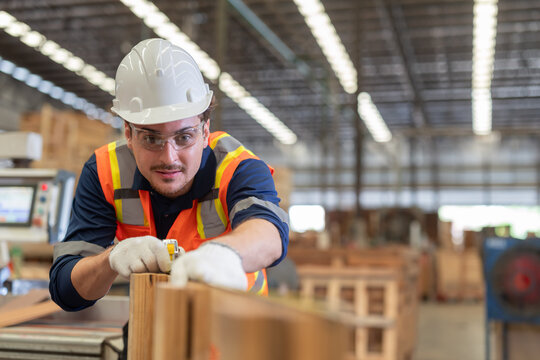 Worker measures wood in a warehouse during the day while wearing safety gear