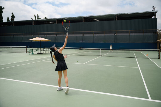 Rear view of Asian Woman Serving on Outdoor Tennis Court During Leisure Match in Daytime