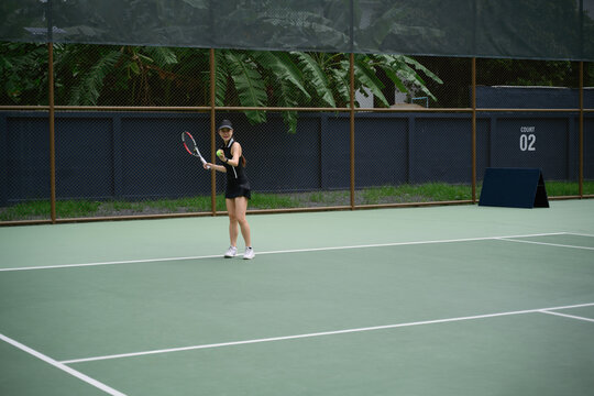 Asian Woman Playing Tennis on Outdoor Court Surrounded by Tropical Greenery