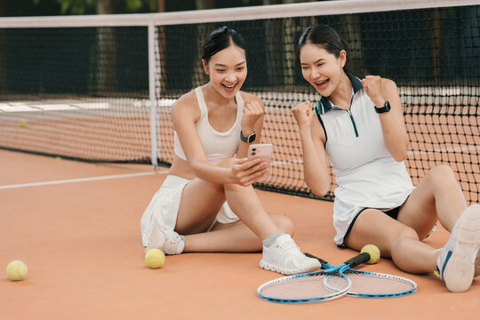 Asian Women Tennis Partners Taking a Break on Court Chatting and Celebrating with Smartphone