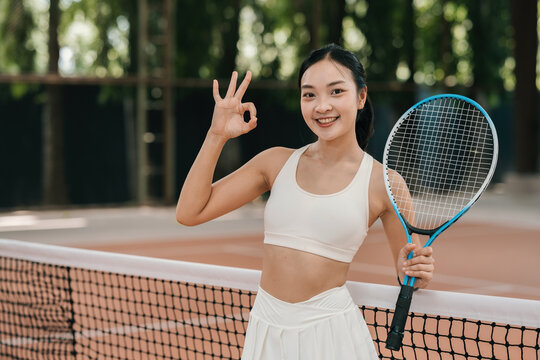 Asian Woman Tennis Player Smiling with OK Gesture Holding Racket on Outdoor Court Portrait
