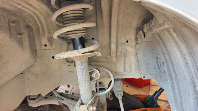Close-up of a dusty car suspension strut assembly with coil spring, showing an automotive shock absorber component for vehicle maintenance, inspection, repair, and mechanical service.