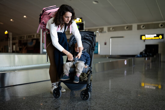Mother fastening child in stroller at airport baggage claim