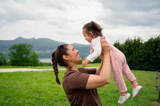 Mother lifting happy daughter playing outdoors in park