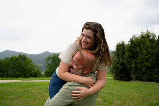 Couple embracing piggyback ride laughing outdoors on grass