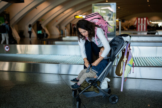Mother securing child in stroller at airport baggage claim