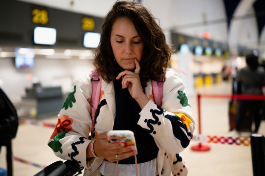 Woman thinking browsing smartphone waiting at airport terminal
