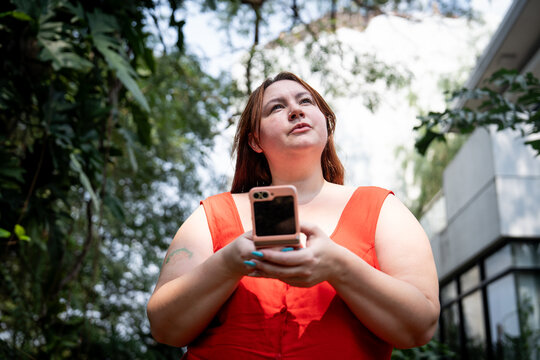 Redhead Gen Z girl with bangs thinking out loud holding a fold phone