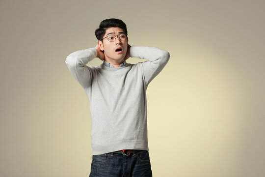 Shocked Young Asian Man with Hands on Head Expressing Surprise