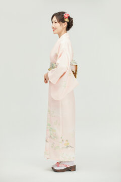 Smiling young Japanese woman in pale pink floral kimono standing in side profile