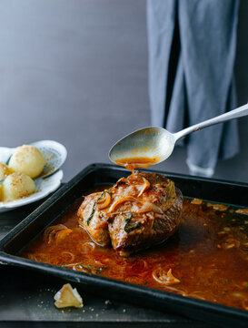 roast of bovine on a baking tray being poured with gravy