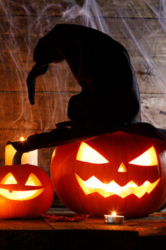 Halloween pumpkins with a witch hat and glowing candles on a wooden background