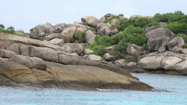 View of Similan Islands rocky coastline with large granite boulders and lush tropical vegetation surrounded by turquoise water in Lam Kaen, Phang Nga, Thailand.
