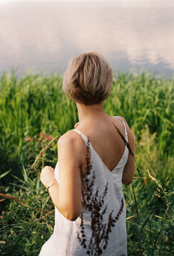 A woman stands at the edge of a still lake in tall reeds