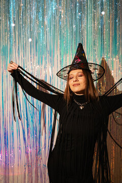 Woman in witch hat posing with arms spread at Halloween party