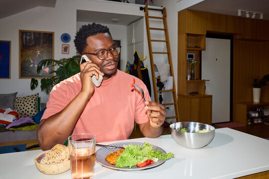 Man eats at home, talking via his phone