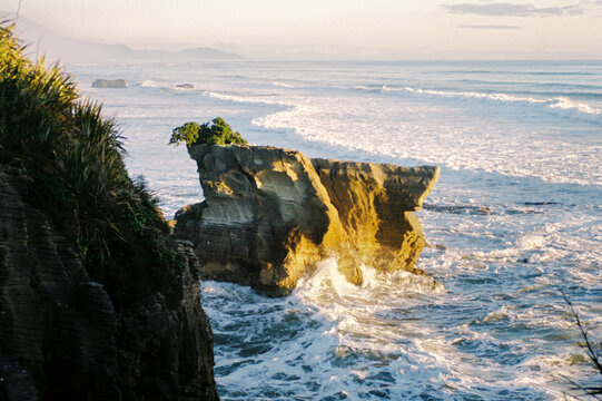 A rocky coast meeting waves under a bright sky in New Zealand
