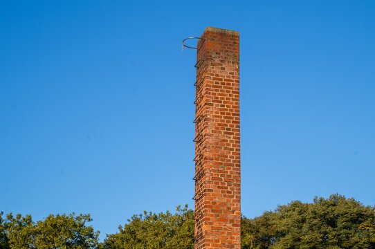 Tall brick chimney with clear blue sky and green trees in background during daylight