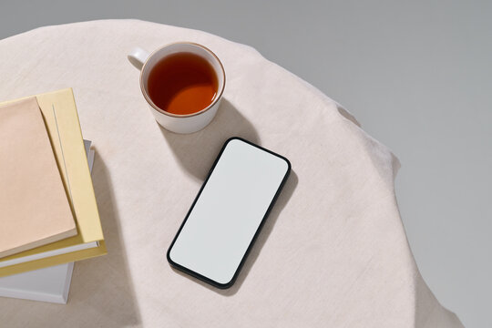 Aesthetic setup with a phone, tea, and books on a cream tablecloth.