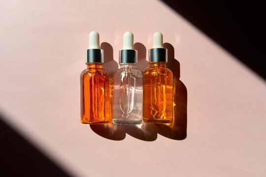 Dropper Bottles with Clear and Orange Serums in Sunlit Pink Background
