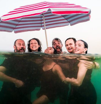 Joyful friends swimming under beach umbrella