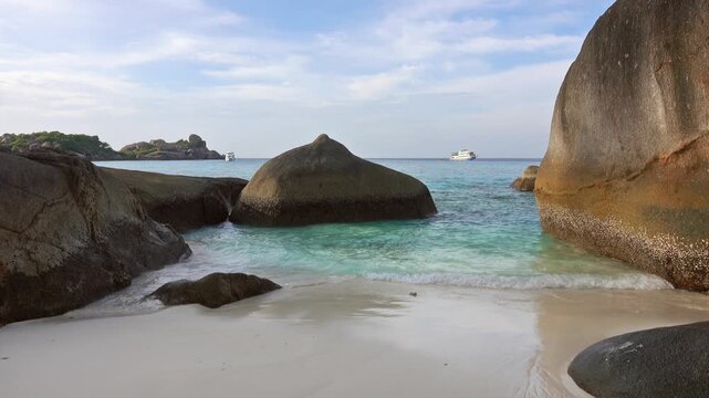 View of Similan Islands beach with large granite boulders, turquoise water, and a boat in the distance in Lam Kaen, Phang Nga, Thailand.