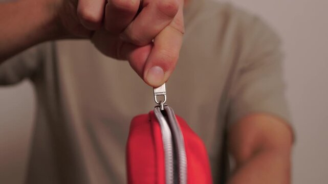 Hands opening pouch. Unzipping red case with care. Person arranging gadgets in soft fabric pouch. Close view of hands organizing electronic accessories in pouch