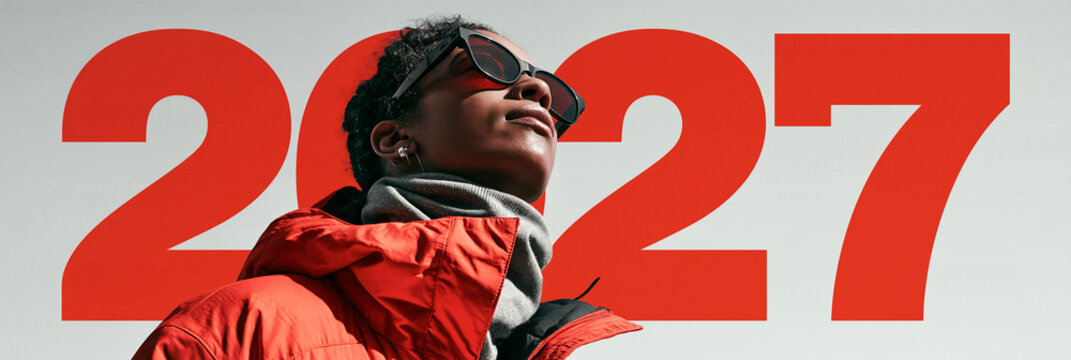 Rote Zahl 2027 mit Frau in orangeroter Jacke und Sonnenbrille
