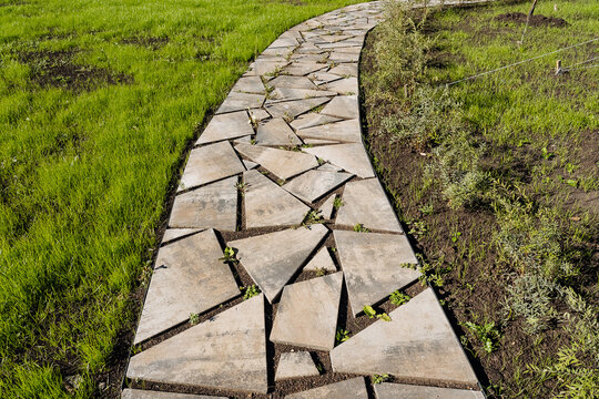 Curved geometric stone pathway winding through fresh green lawn with irregular slabs, bright grass border, and new planting beds under crisp sunlight for frontyard landscaping