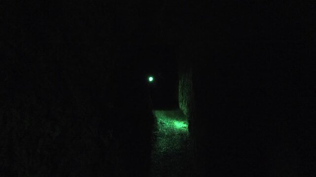 Researcher walks deep inside cave passage, lone explorer moving through dark underground chamber.