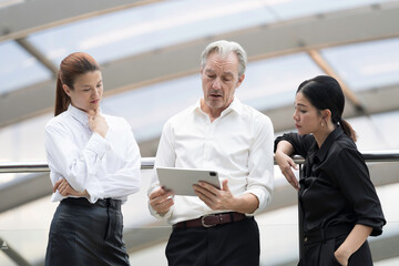 Fototapeta premium Group of business team, manager, diverse corporate colleagues brainstorming, discuss project together with digital tablet at outside office within the building complex
