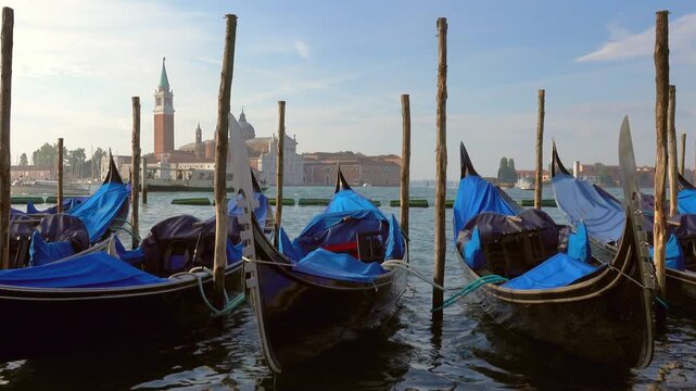 View of traditional gondolas moored at wooden poles in the lagoon with the San Giorgio Maggiore church in the background in Venice, Veneto, Italy.