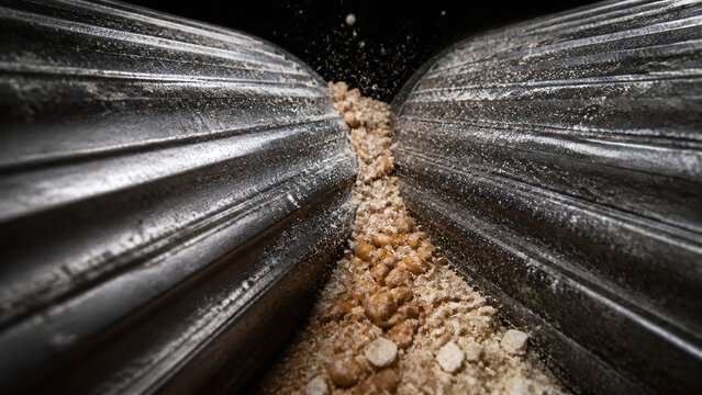 Extreme close-up of fluted metal rollers crushing wheat kernels into meal in a flour mill.